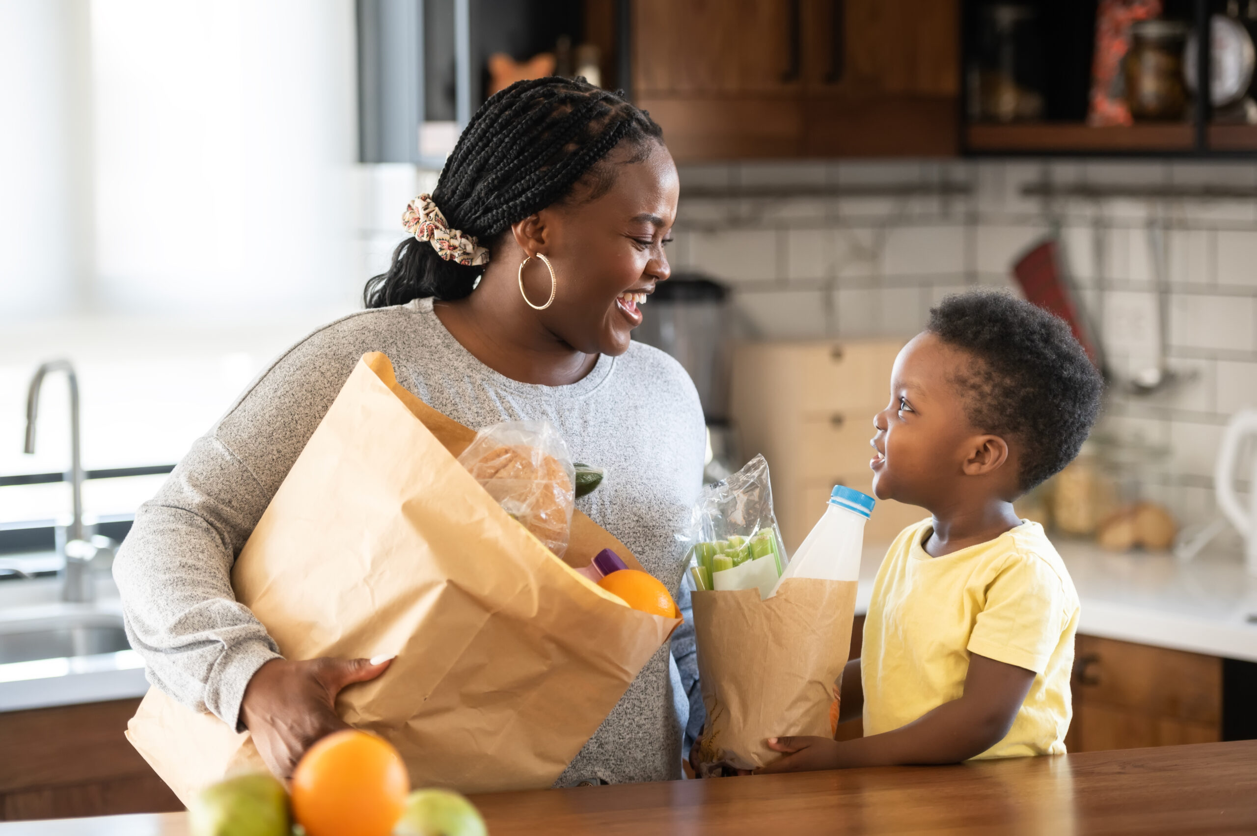 Cheerful African-American mother and son in the kitchen. Son helps a mother to bring in groceries after a grocery-shopping Cheerful African-American mother and son in the kitchen. Son helps a mother to bring in groceries after a grocery-shopping